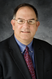Photo of Prof. Mark Sidel, in black suit with maroon tie in front of grey background.