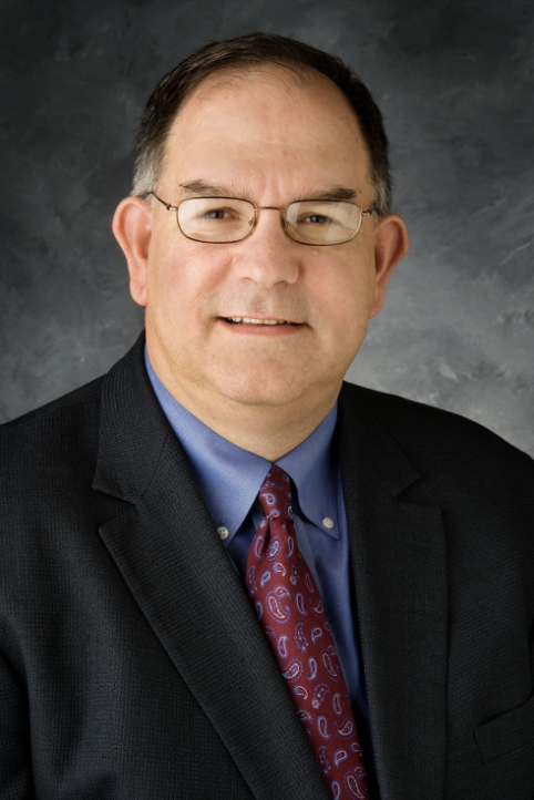 Photo of Prof. Mark Sidel, in black suit with maroon tie in front of grey background.
