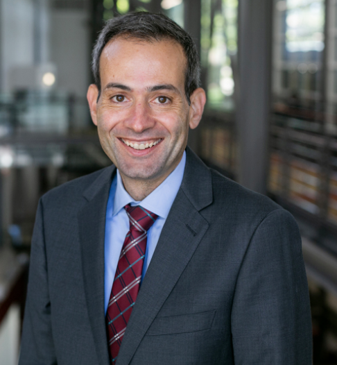 Photo of Professor Yaron Nili. He is wearing a grey suit and a blue shirt with a red tie.